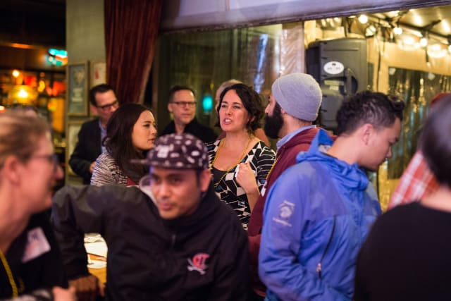 Group of diverse attendees engaging in conversation at the Love Bomb 2017 event, supporting My Voice Music nonprofit, with a lively atmosphere in a Portland venue.